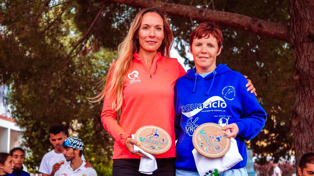Two women proudly display awards at an outdoor sports event.